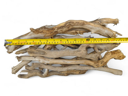 Pile of weathered, light brown and gray driftwood sticks measured by a yellow tape on white.