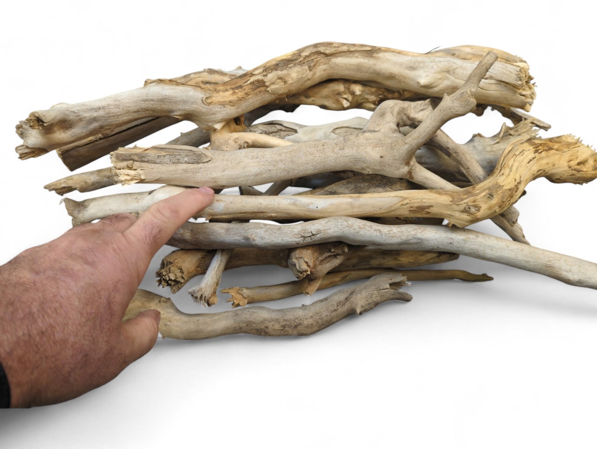 A human hand points at a pile of natural, weathered driftwood sticks in light brown and gray.