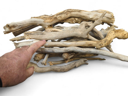 A human hand points at a pile of natural, weathered driftwood sticks in light brown and gray.