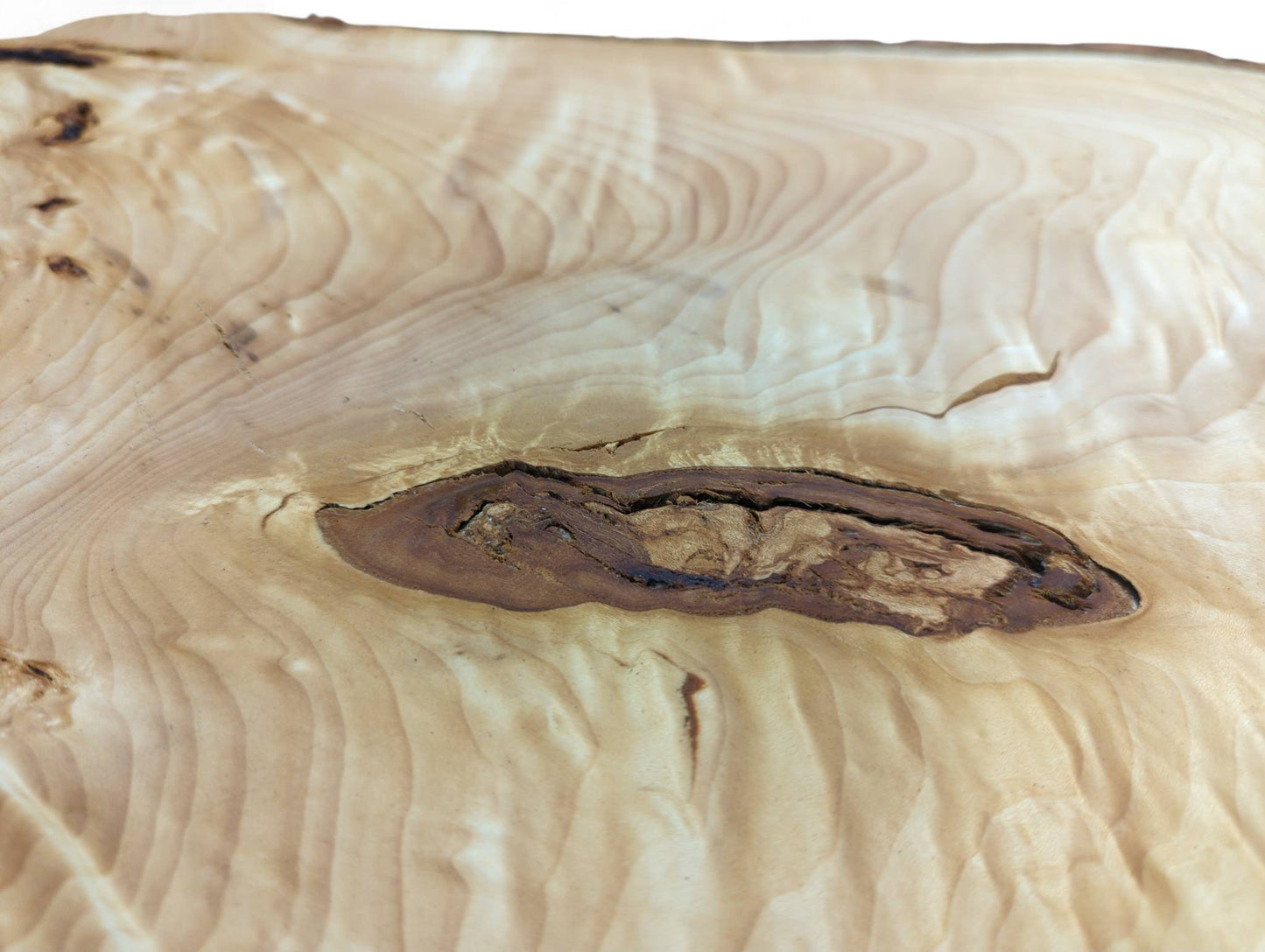 Highly figured linden root wood, light-colored, with strong swirling grain and a dark, elongated inclusion.