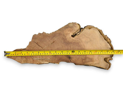 A light brown wild cherry wood slab displays natural live edges, prominent cracks, and a yellow measuring tape.