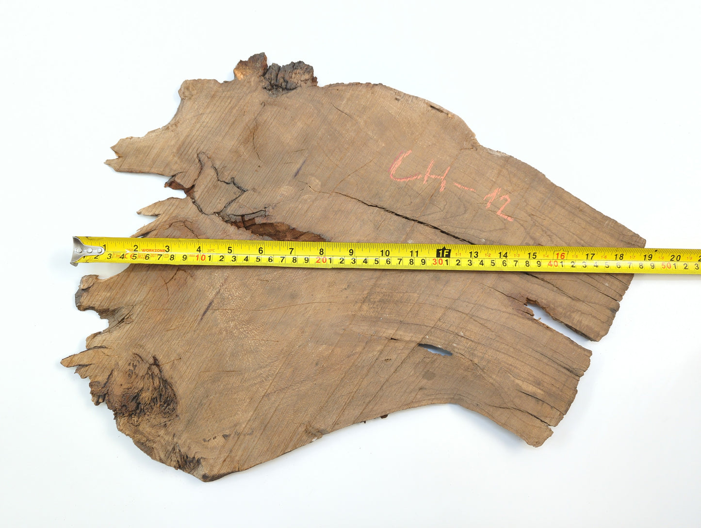 An overhead view of a raw cherry slab with a yellow tape measure demonstrating its width.