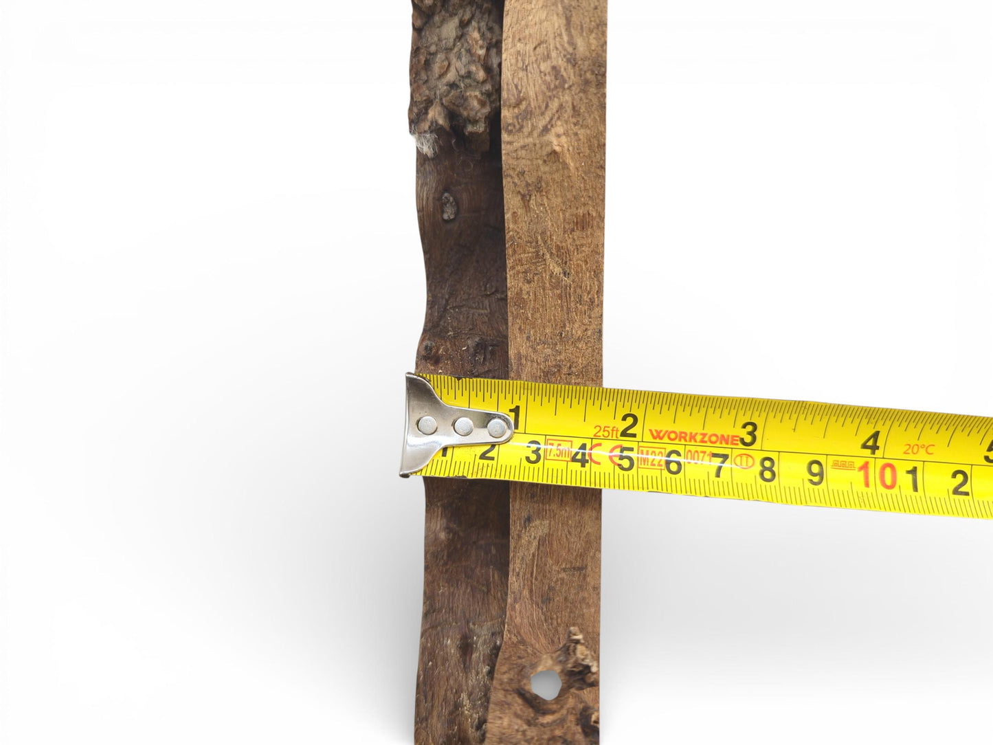 A yellow tape measure is held across the rough edge of a wood slab, indicating its thickness.