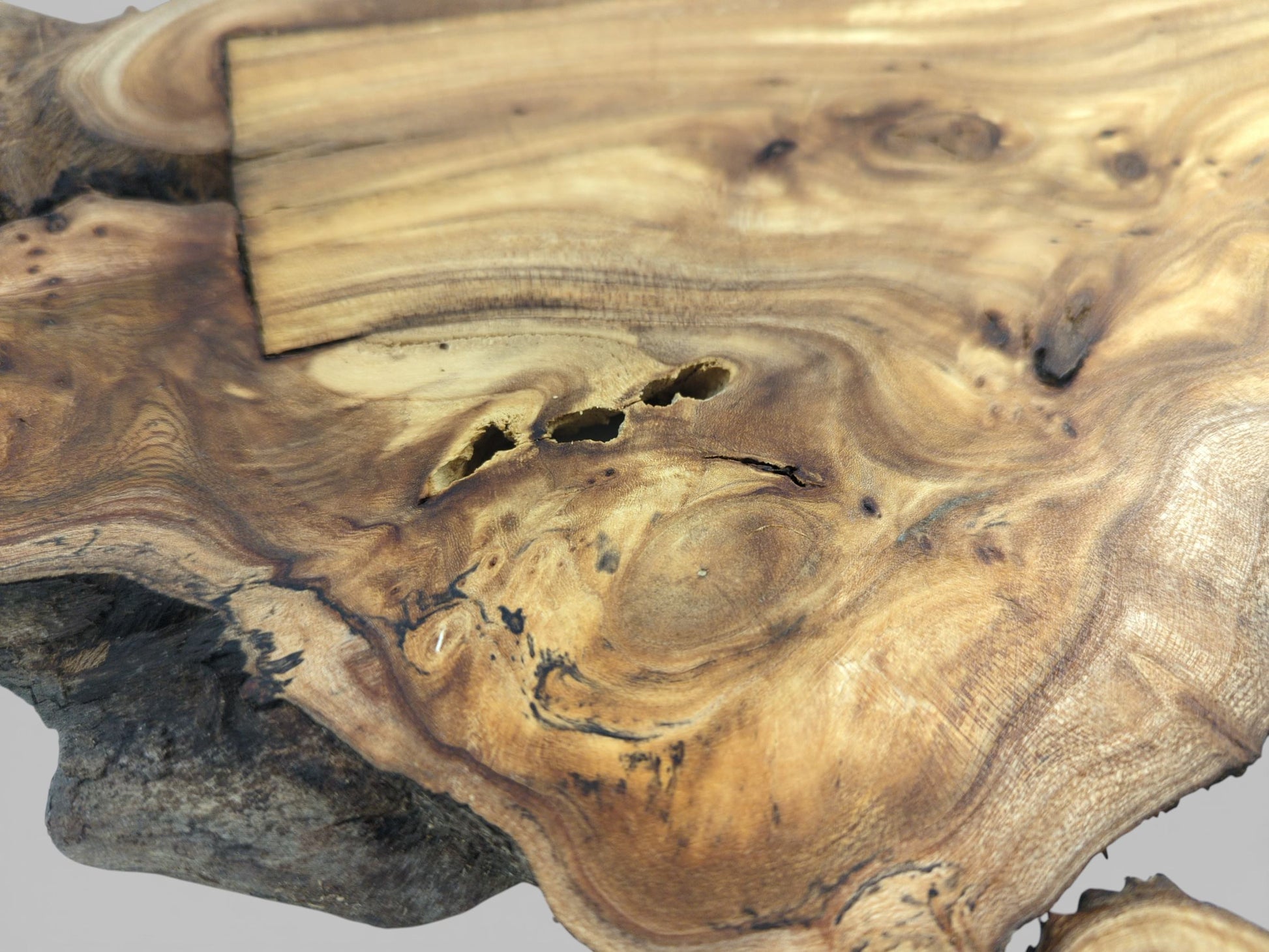 A detailed view of a wood slab's surface with swirling grain, central voids, and a rectangular inlay.