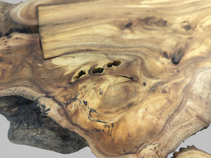 A detailed view of a wood slab's surface with swirling grain, central voids, and a rectangular inlay.