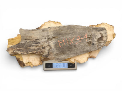 A collection of raw, irregular wood pieces placed on a small digital scale showing their weight.