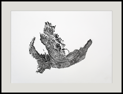 An irregular black tree root monoprint with visible growth rings, matted in light grey and framed in black.