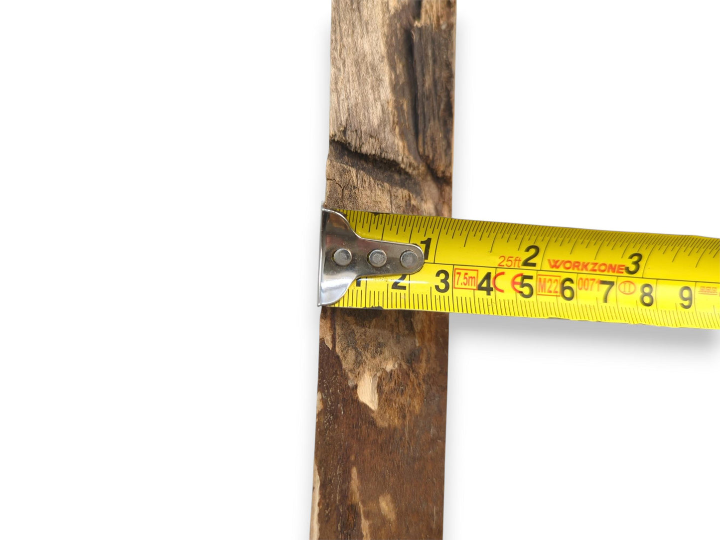 A metal-tipped tape measure gauges the width of a dark, weathered timber slab's edge.