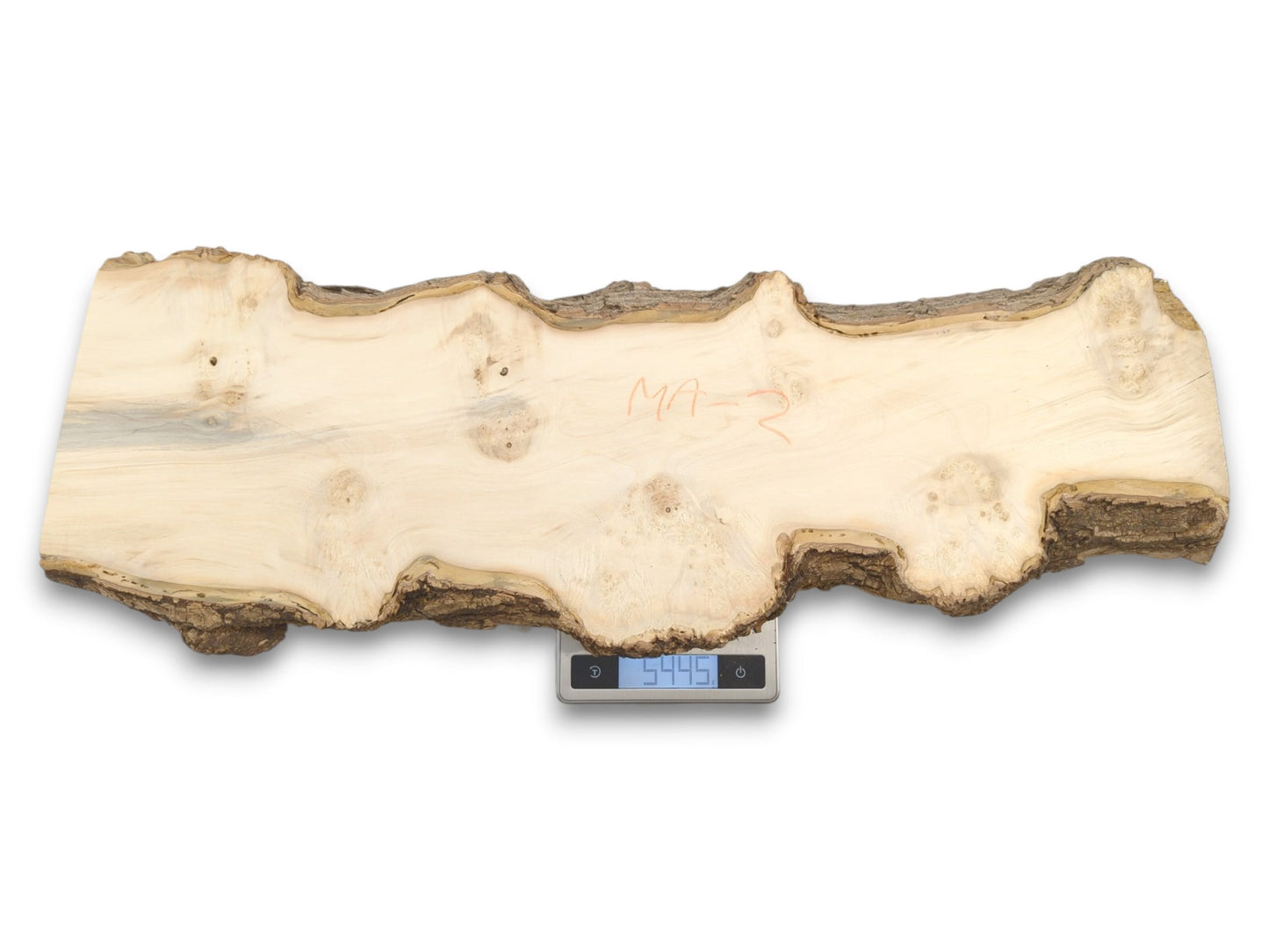 A pale, live-edge lumber slab with red crayon writing sits on a digital scale.