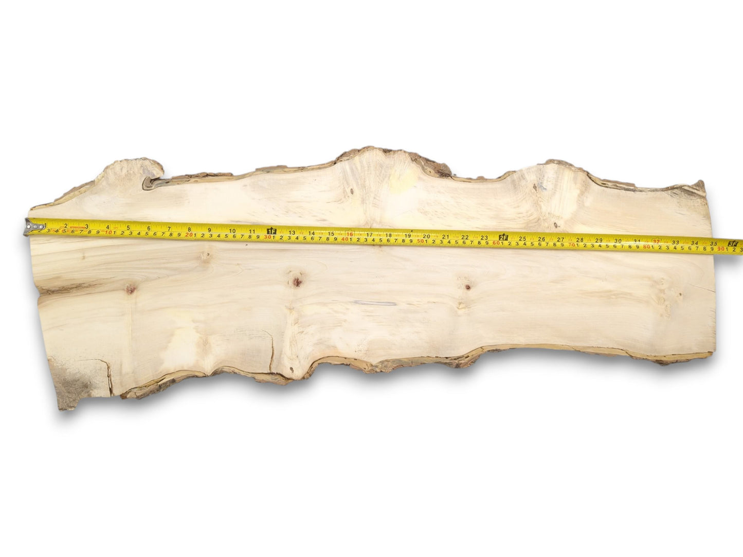 A yellow tape measure stretches across a long, pale wood plank with natural, uneven edges.