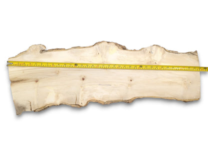A yellow tape measure stretches across a long, pale wood plank with natural, uneven edges.