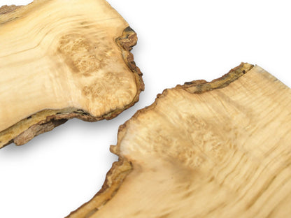Two pale timber blanks with knotty burl eyes and rugged live edges face each other.