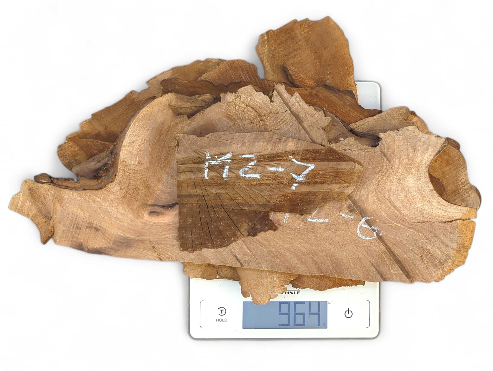 Pile of raw, irregularly shaped walnut wood slices with handwritten labels on a digital scale displaying 964g.