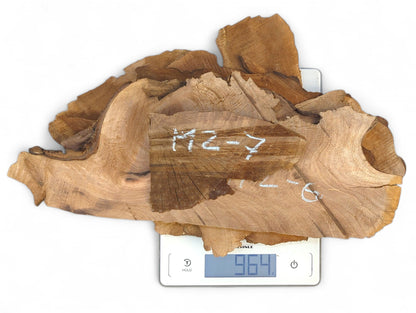 Pile of raw, irregularly shaped walnut wood slices with handwritten labels on a digital scale displaying 964g.