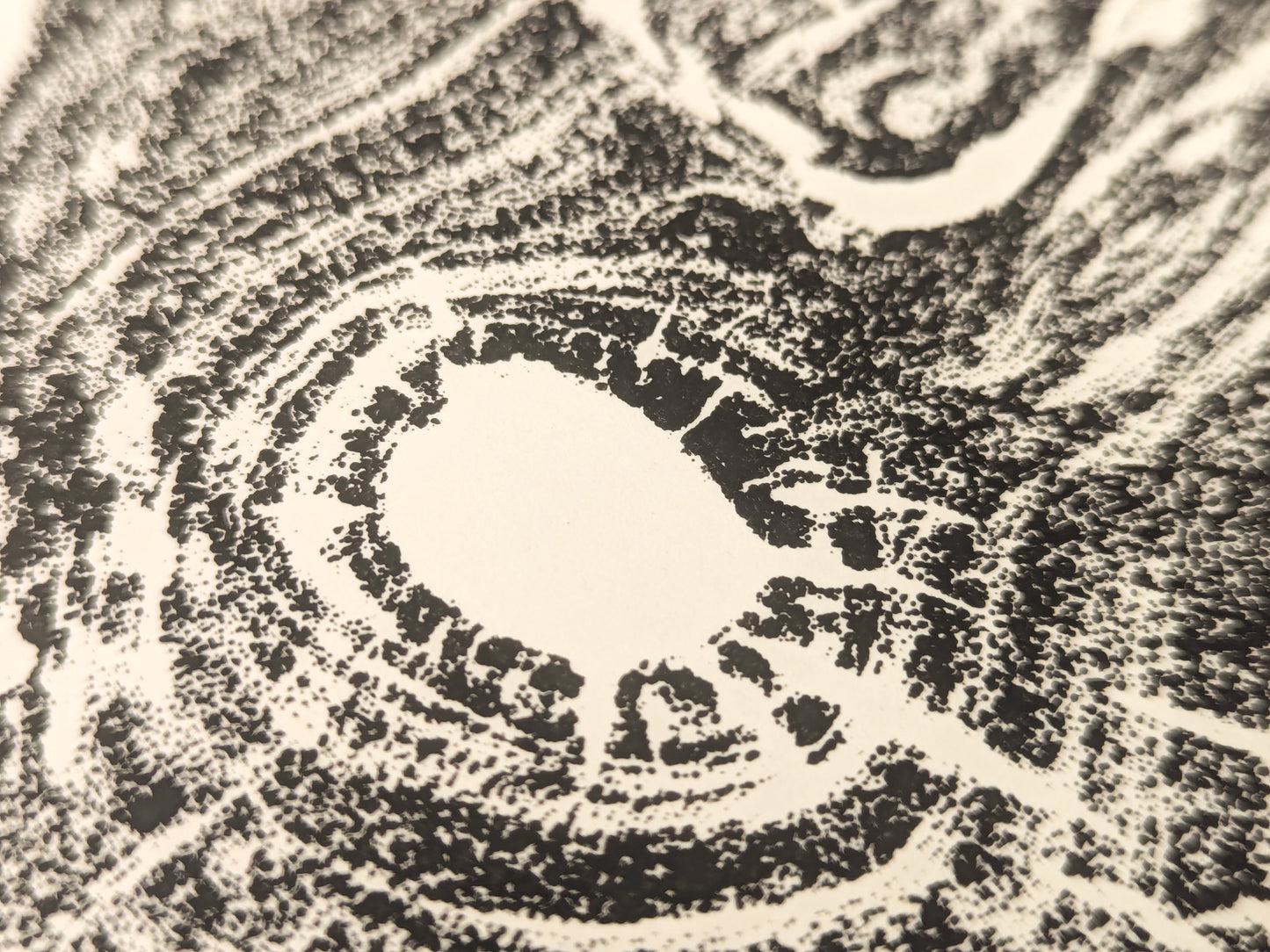 Textured black impression of an irregular tree root slice with granular concentric patterns on cream paper.