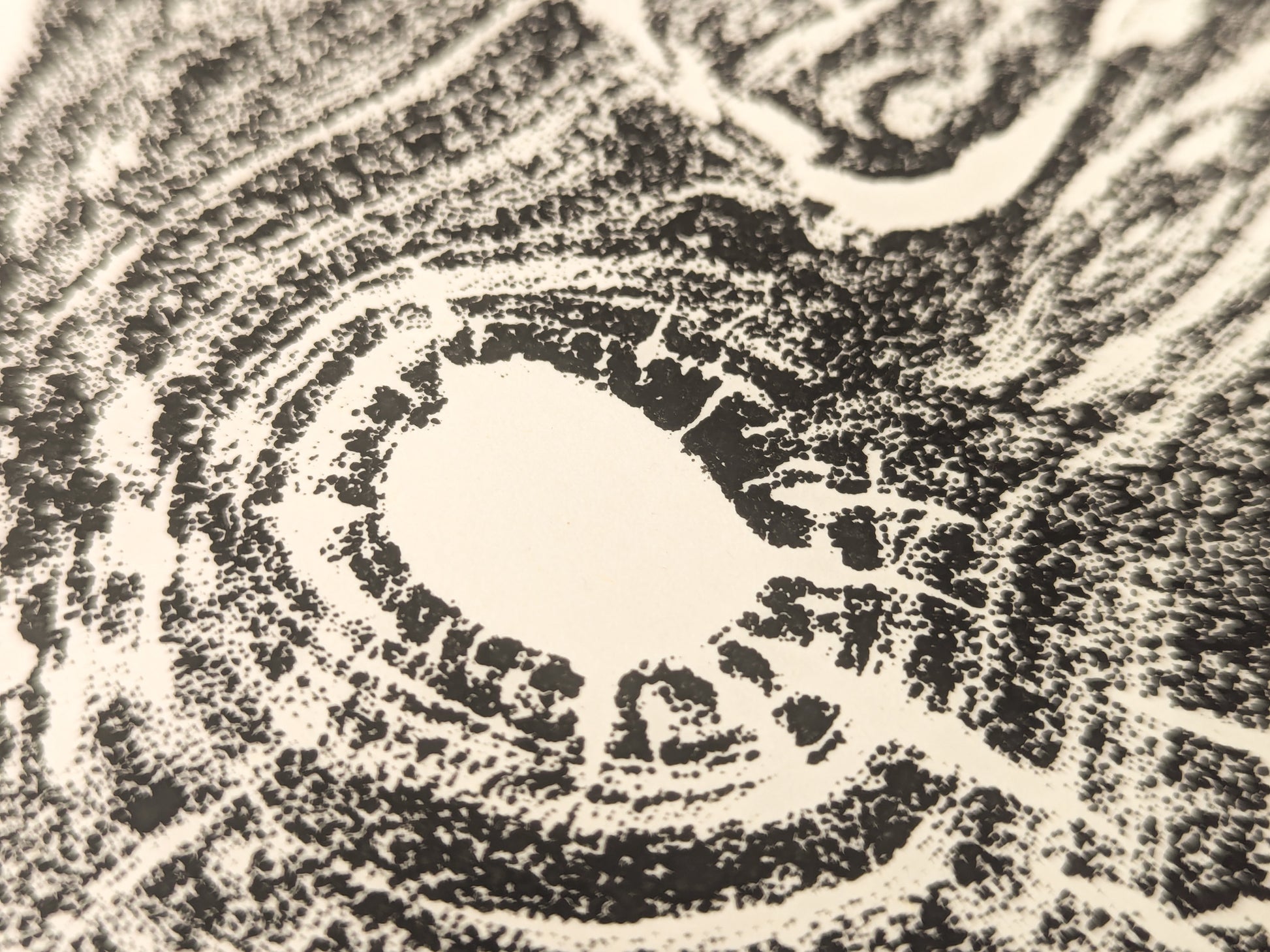Textured black impression of an irregular tree root slice with granular concentric patterns on cream paper.