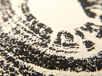 Irregular black granular ink forms a tree root slice impression on cream-colored paper.