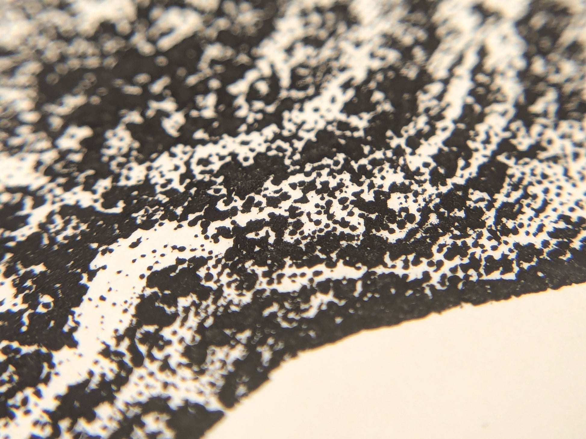 Magnified view of a textured black ink monoprint impression with granular irregular patterns on cream-colored paper.