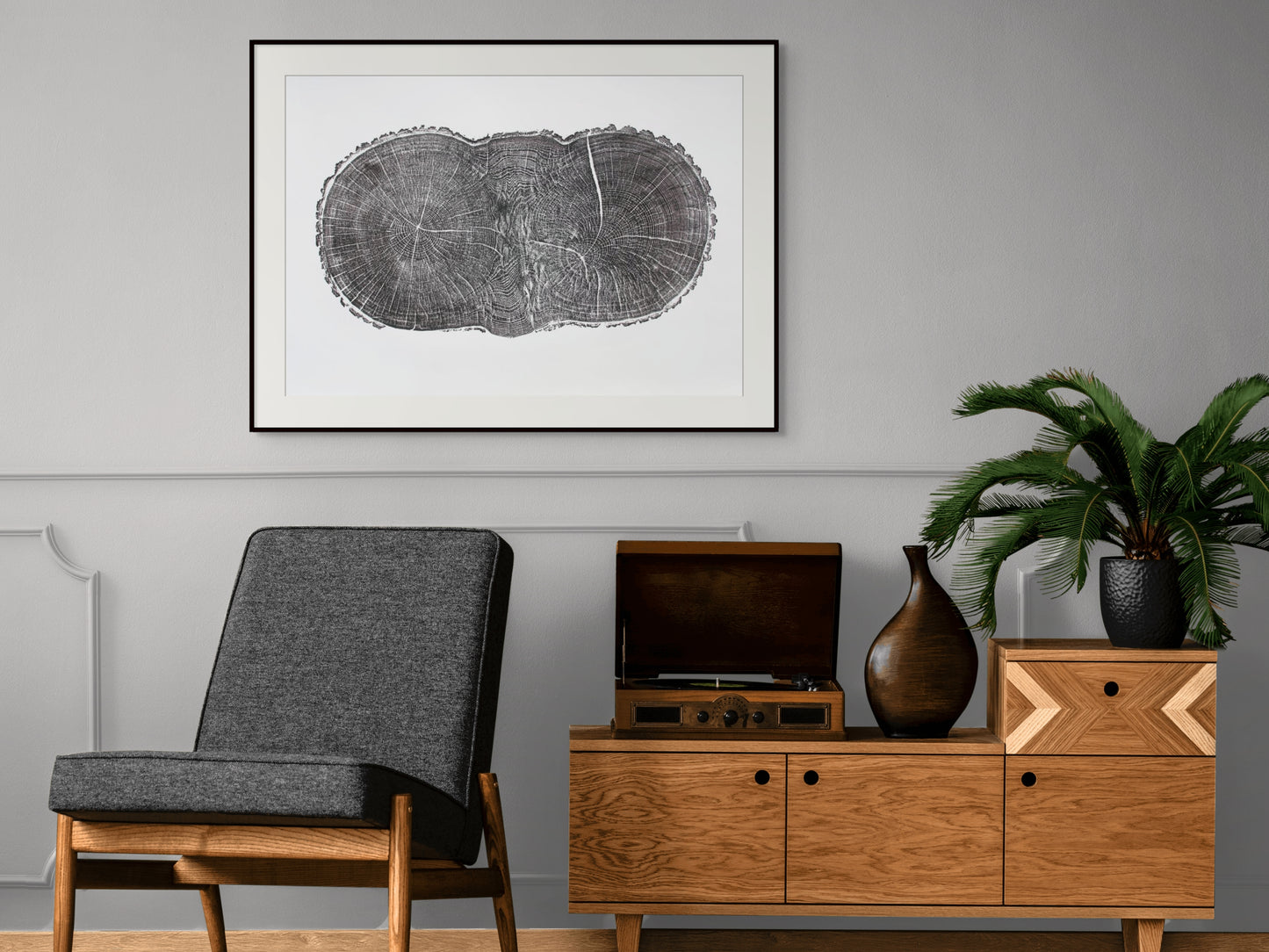 A framed oak tree ring print is centered above a grey chair and wooden console.