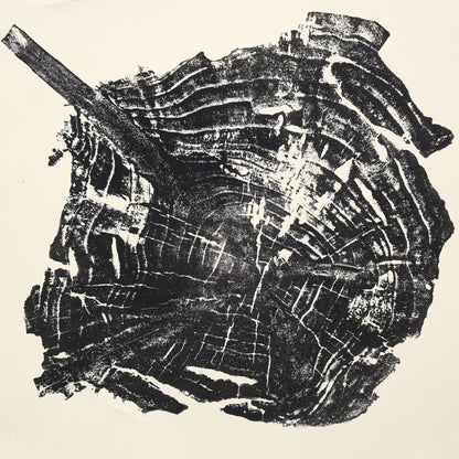 Organic woodcut monoprint displays an irregular black tree root slice, showing concentric rings and a diagonal branch.