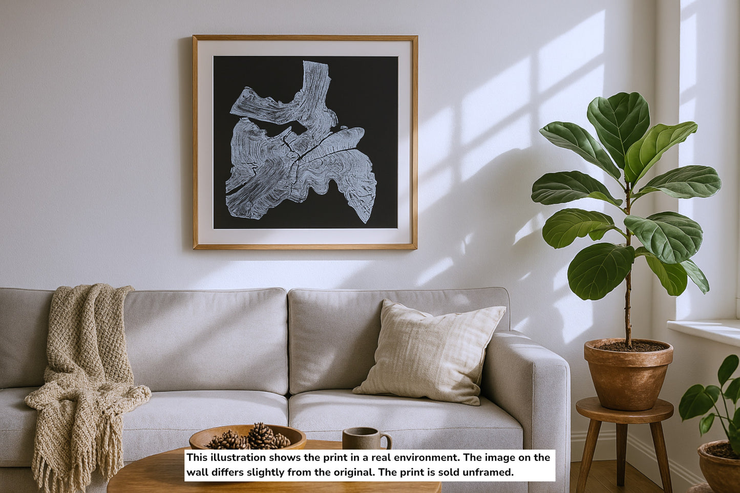 A framed monoprint of a white irregular tree root impression on black, displayed above a couch.