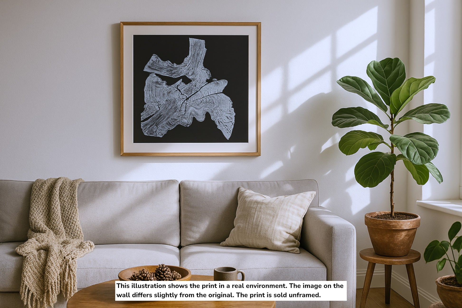 A framed monoprint of a white irregular tree root impression on black, displayed above a couch.