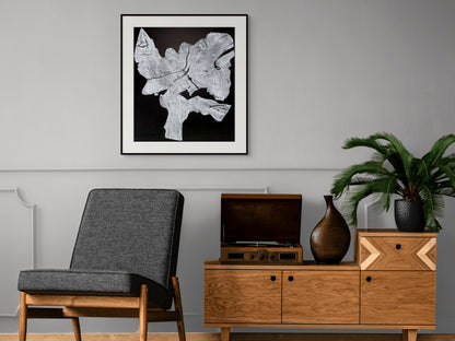 Framed black and white woodcut root print on gray wall above dark chair and wooden credenza.