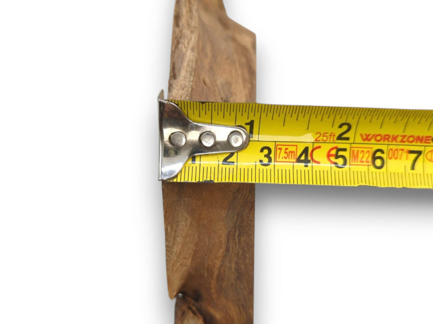 A close-up on the edge of a wood slab, its thickness verified by a yellow tape measure.