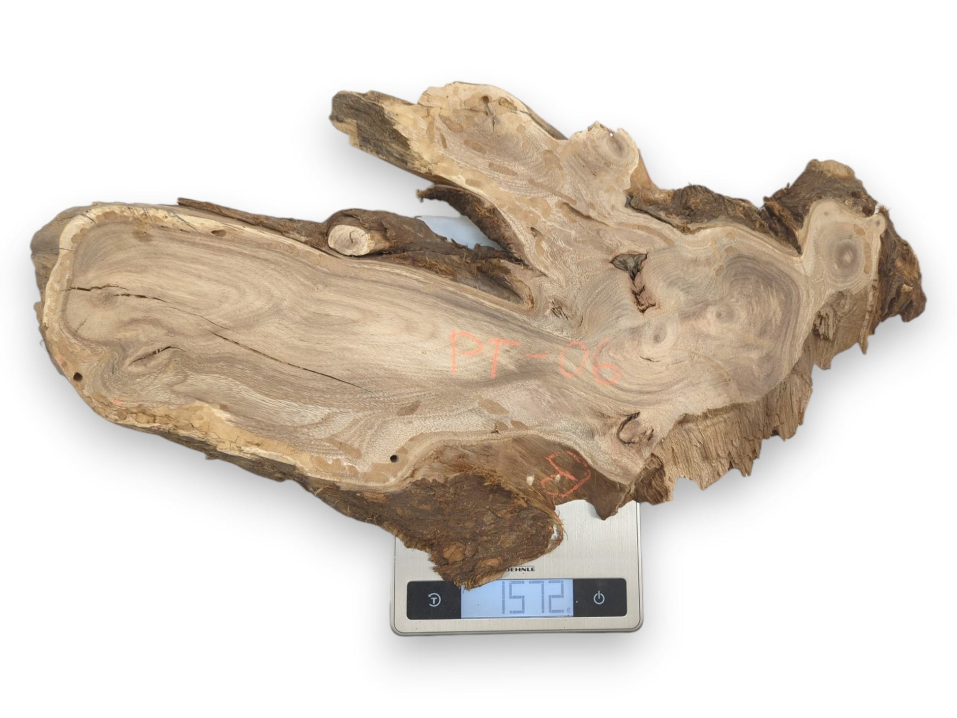 An irregular, live-edge wood slab with swirling grain is weighed on a digital scale.