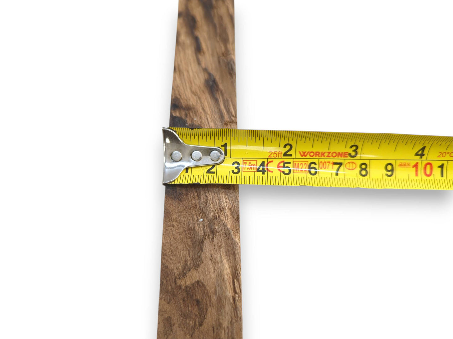 A yellow tape measure gauges the width of a timber plank with dark, linear grain.