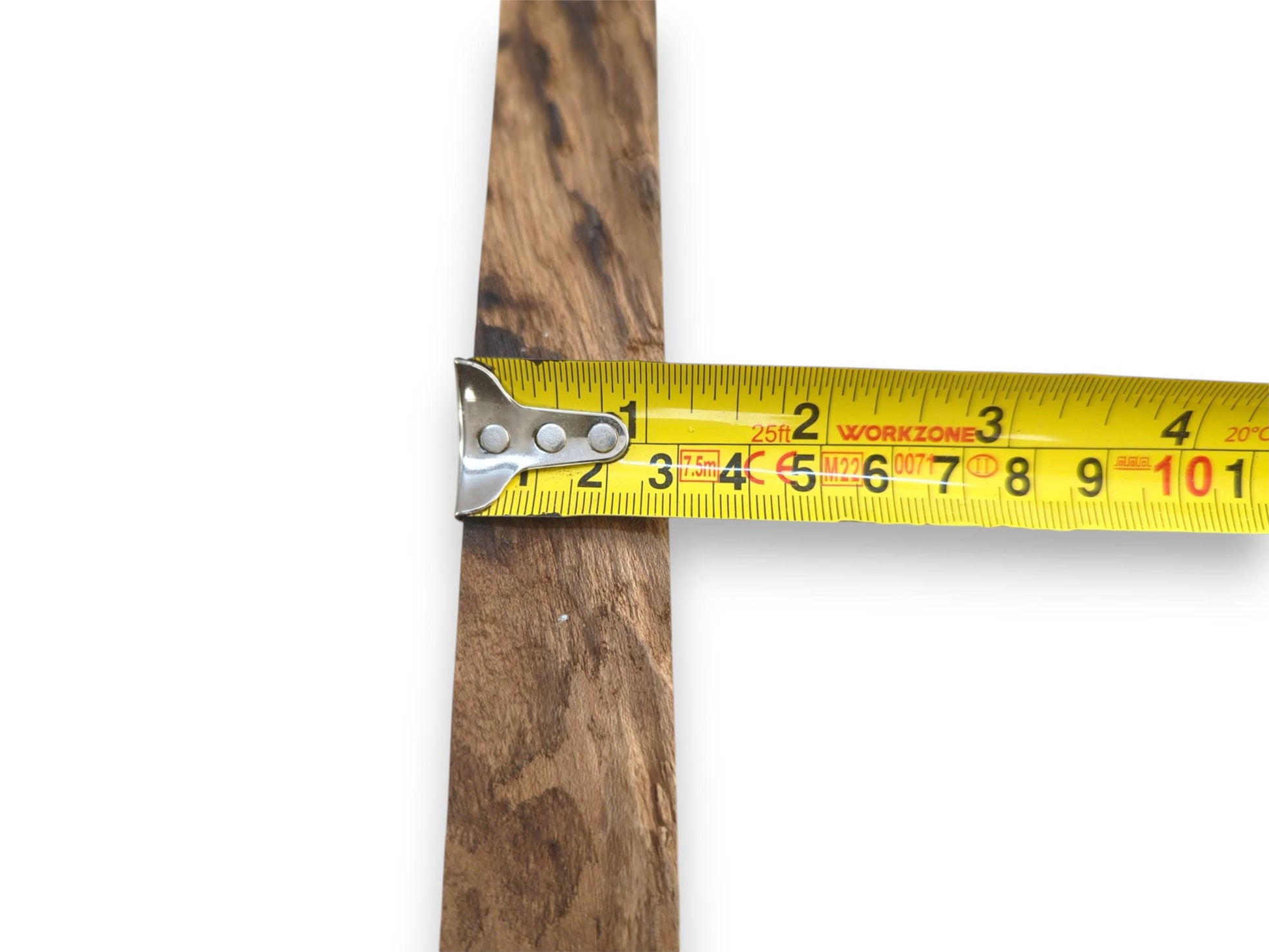 A yellow tape measure gauges the width of a timber plank with dark, linear grain.