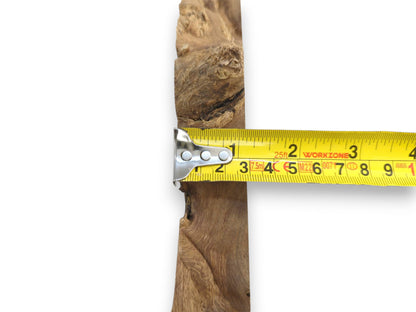 A measuring tape's metal end presses against the rugged, fibrous edge of a timber piece.