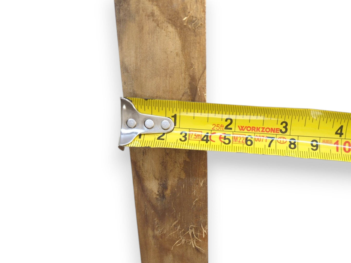 A yellow tape measure gauges the thickness of a raw, fibrous plank against a white background.