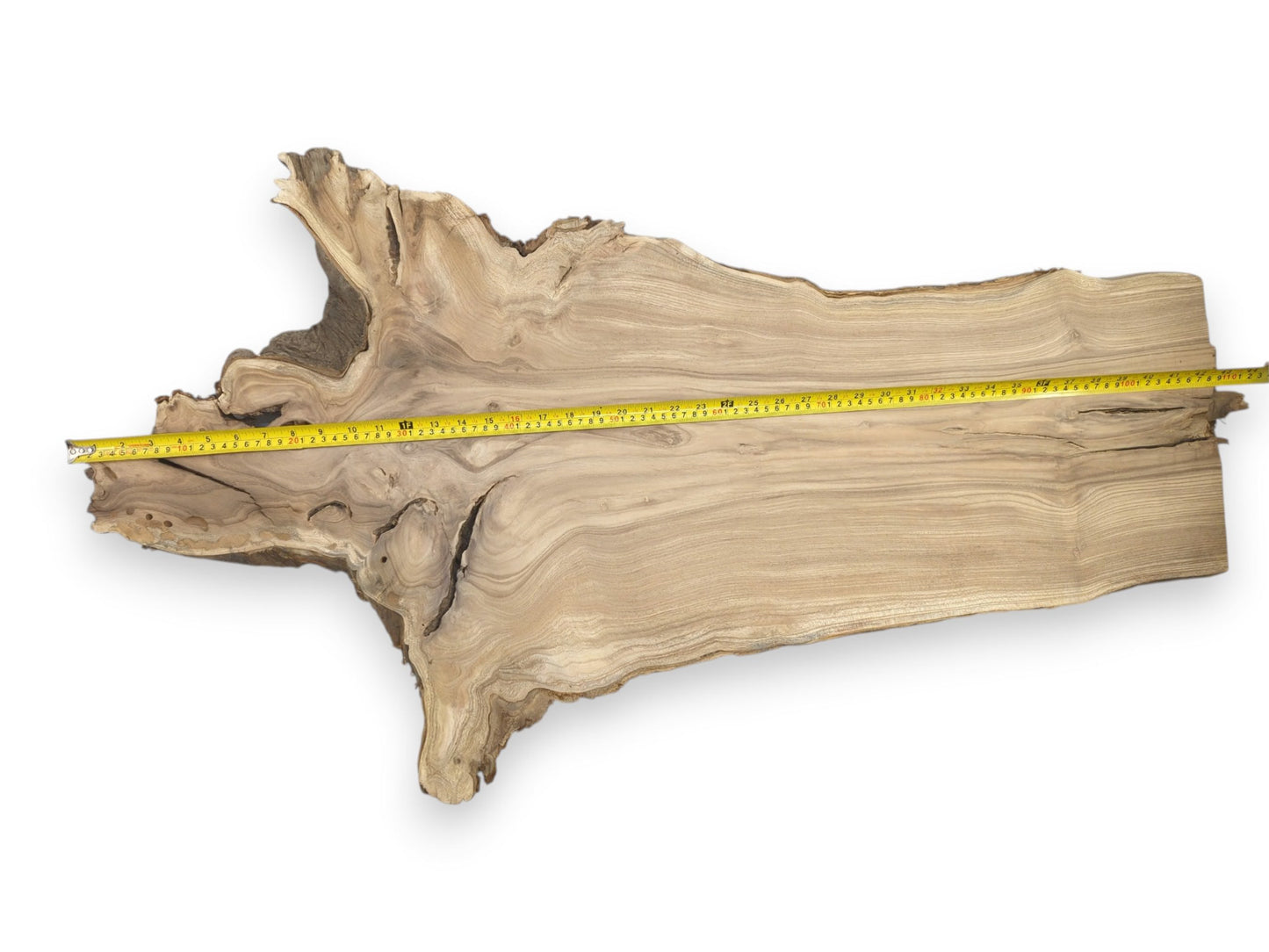 A yellow measuring tape is stretched across a long, raw timber plank with irregular edges.