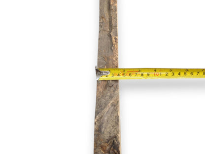 A yellow measuring tape is held across a narrow timber plank with a rough surface.