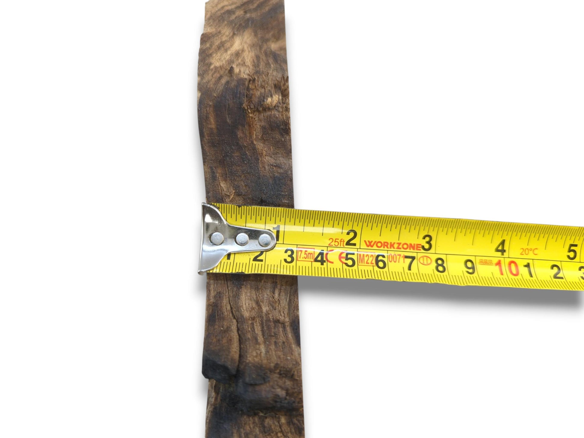 A bright yellow measure crosses a dark, coarse-textured wood cutting with an irregular edge.