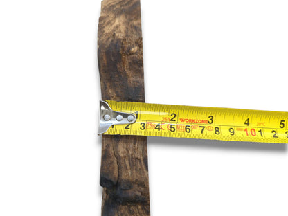 A bright yellow measure crosses a dark, coarse-textured wood cutting with an irregular edge.