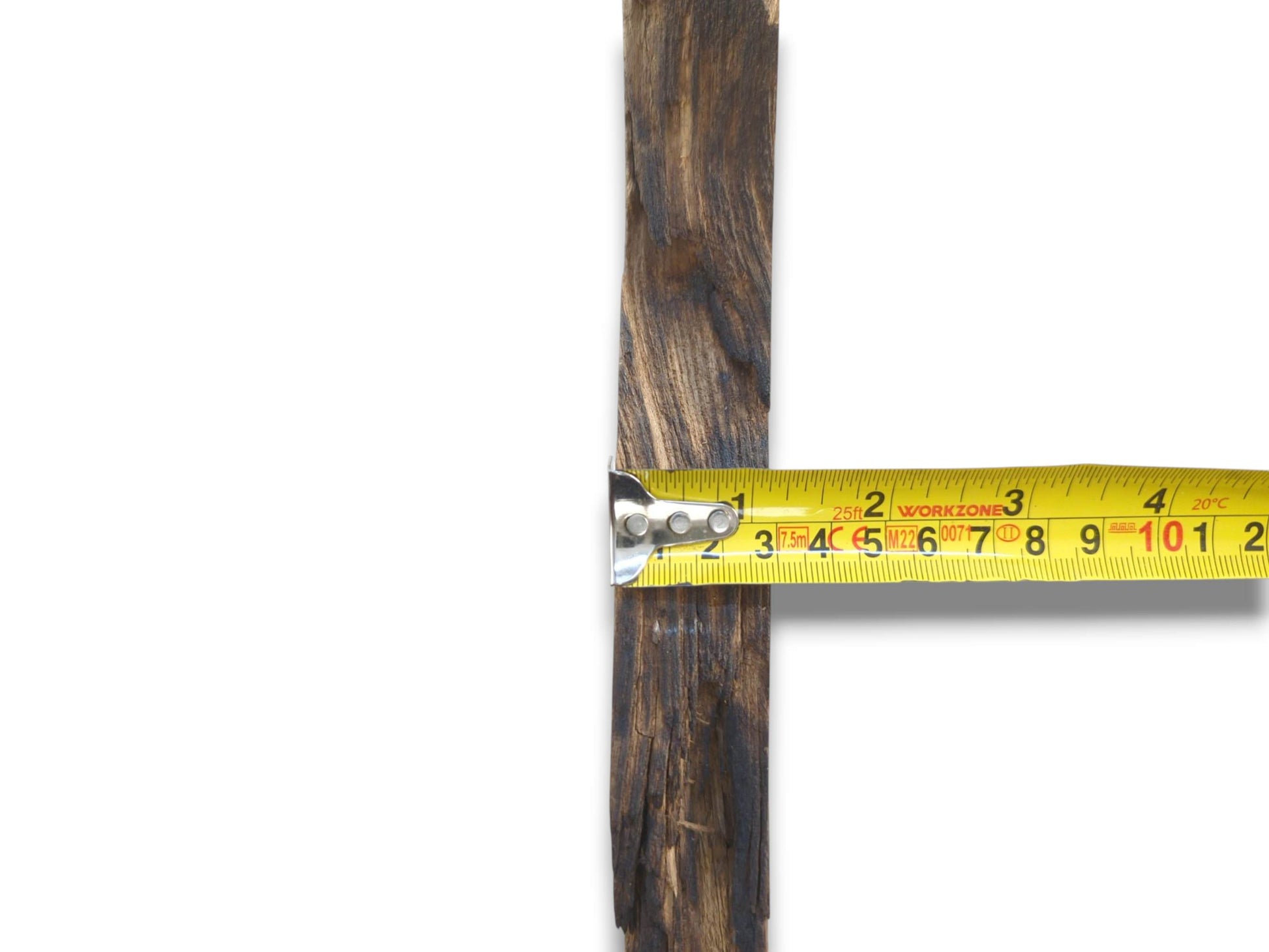 A yellow tape measures the width of a dark, charred-looking timber piece with deep grooves.