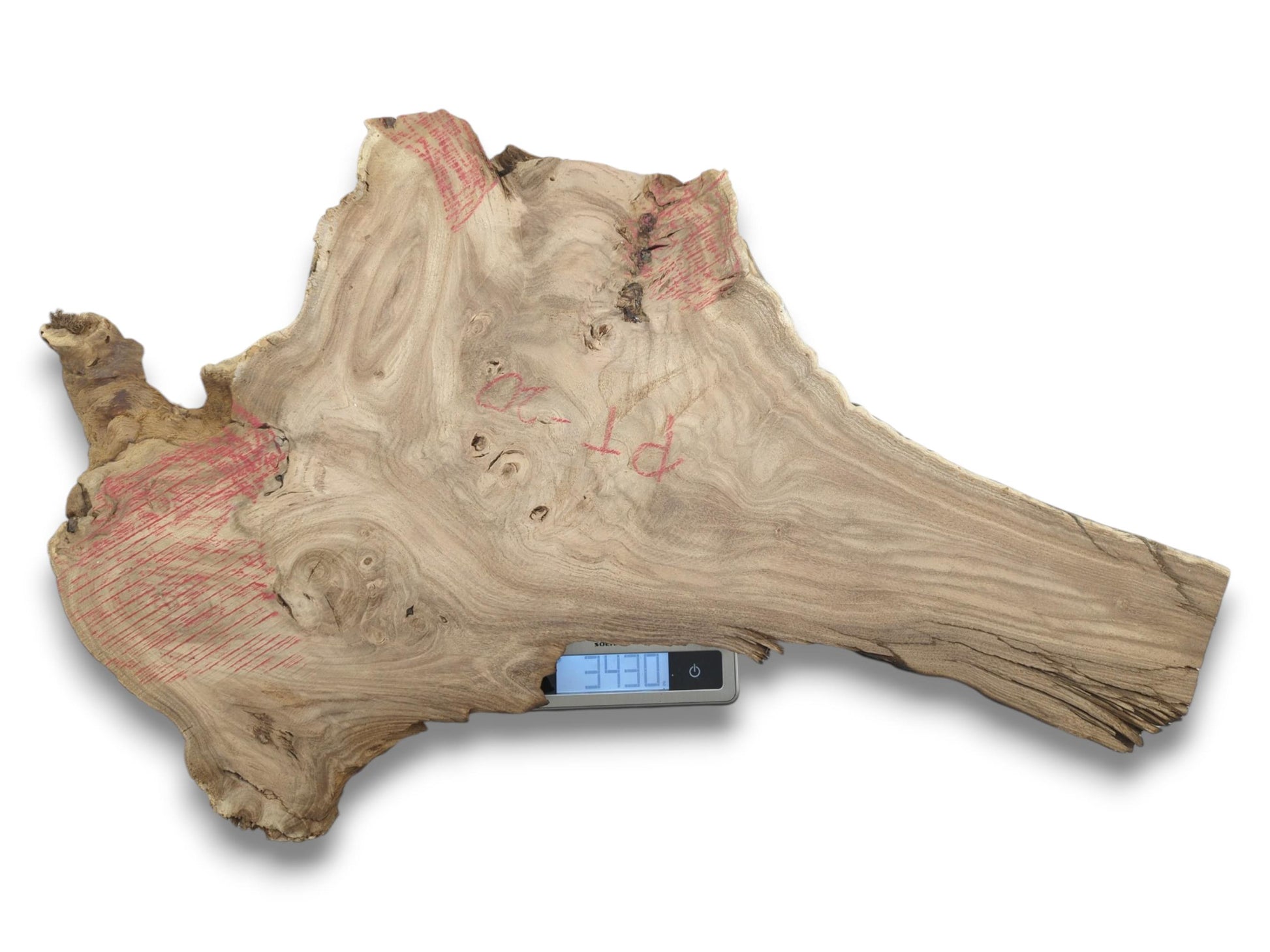 A raw timber slab with swirling grain and red marks is weighed on a scale.