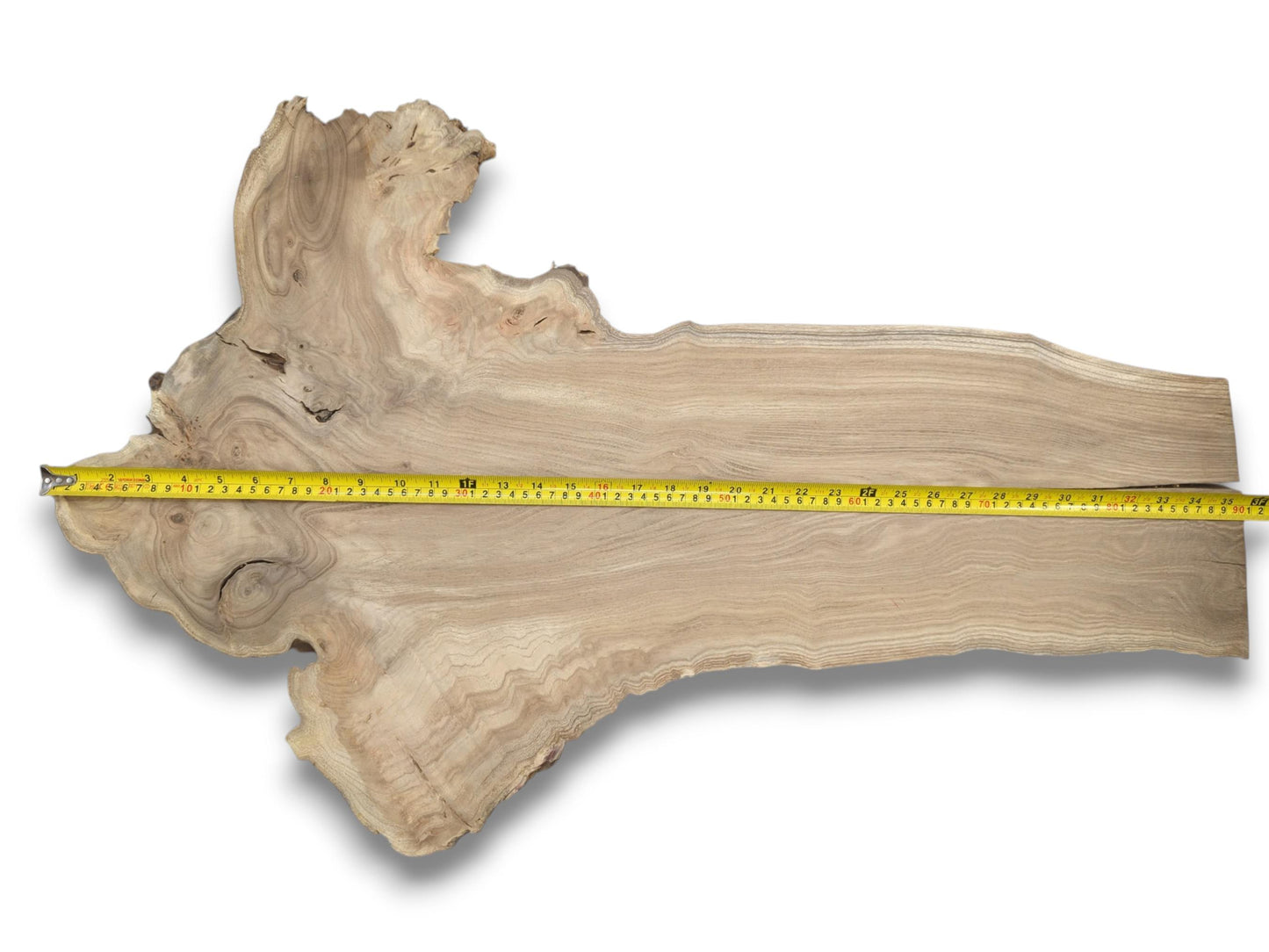 A yellow measuring tape spans a long, irregular wood plank with a gnarled, knotty end.