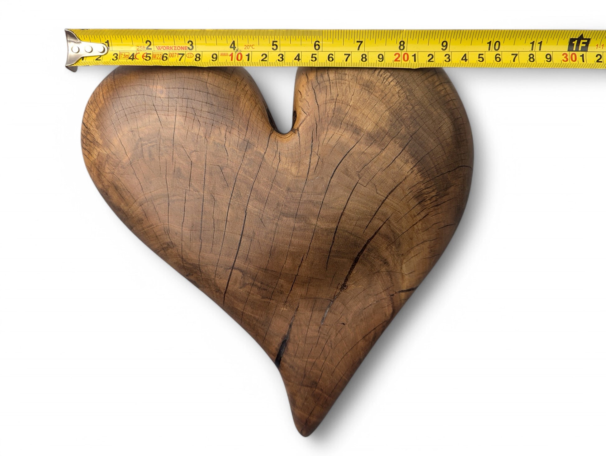 Hardwood heart sculpture, with natural grain and visible cracks, measured by yellow tape showing 9 inches.