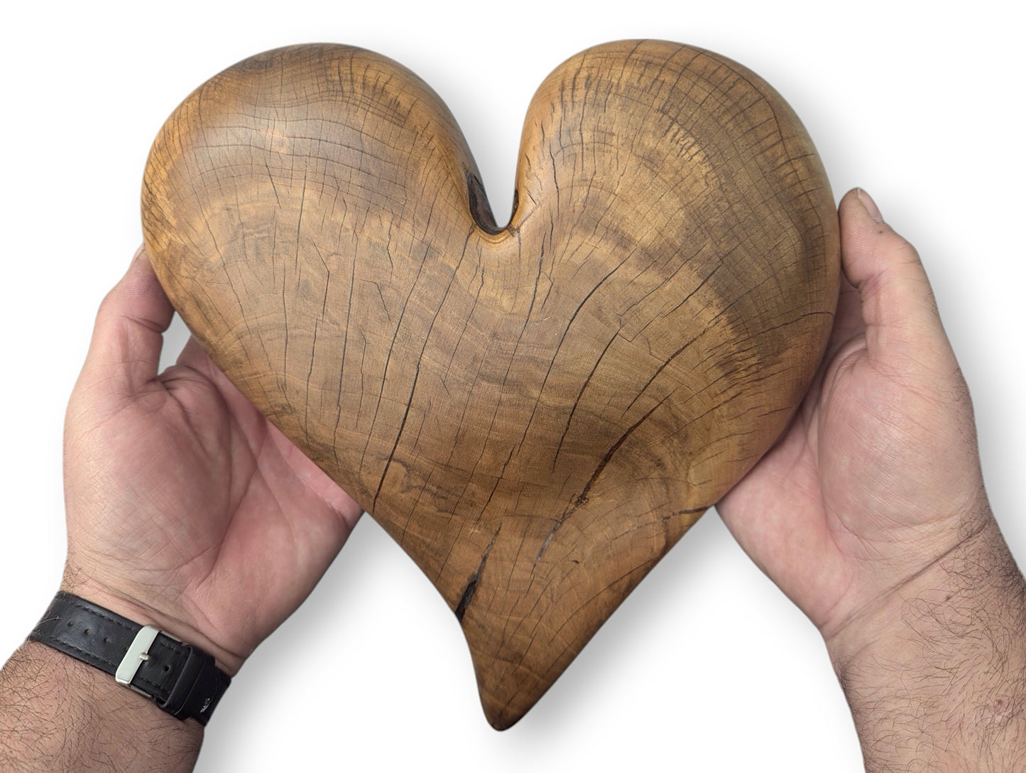Two hands hold a brown, heart-shaped wood sculpture, featuring natural grain, fine cracks, and an oiled finish.