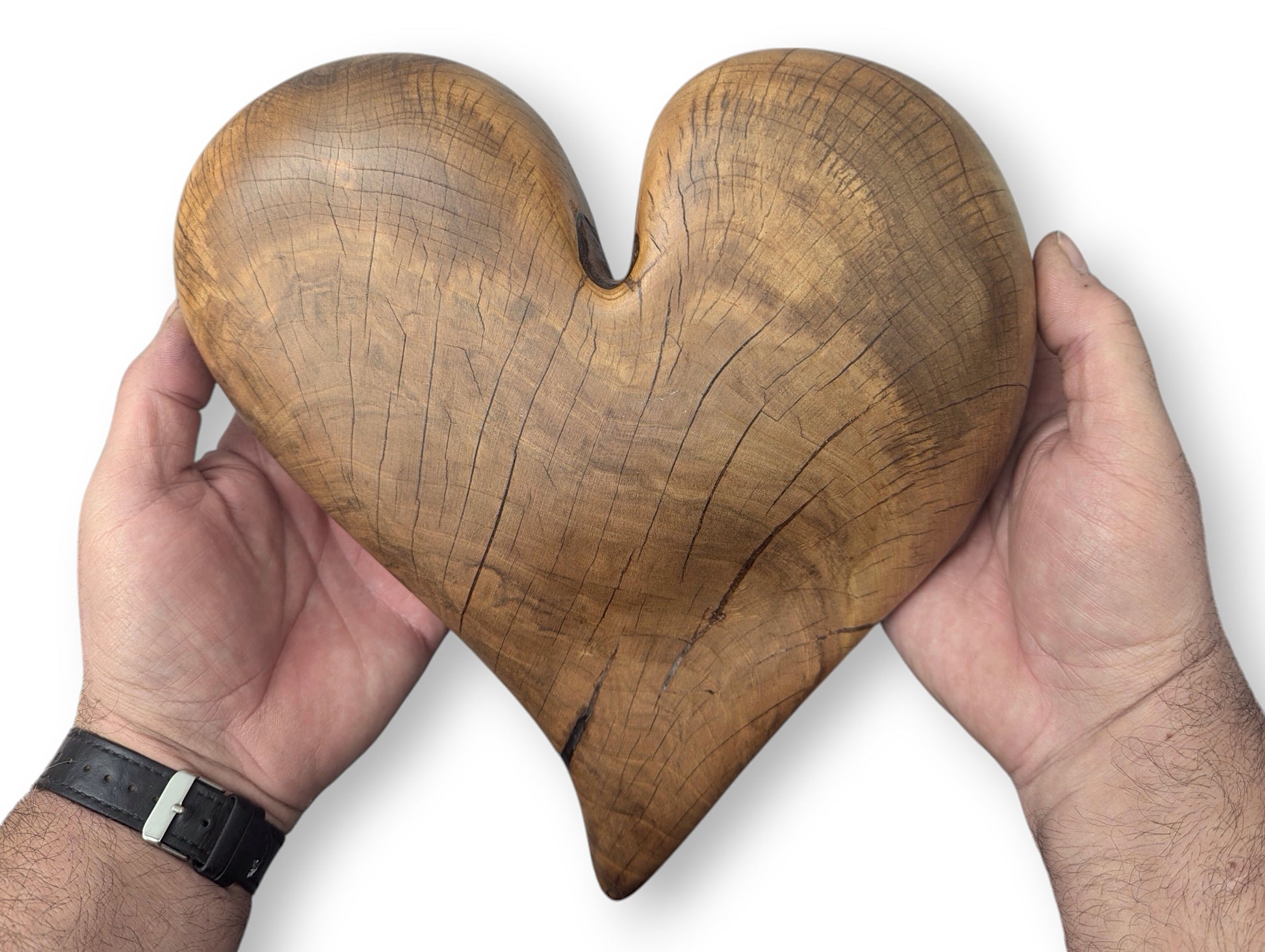Two hands hold a brown, heart-shaped wood sculpture, featuring natural grain, fine cracks, and an oiled finish.