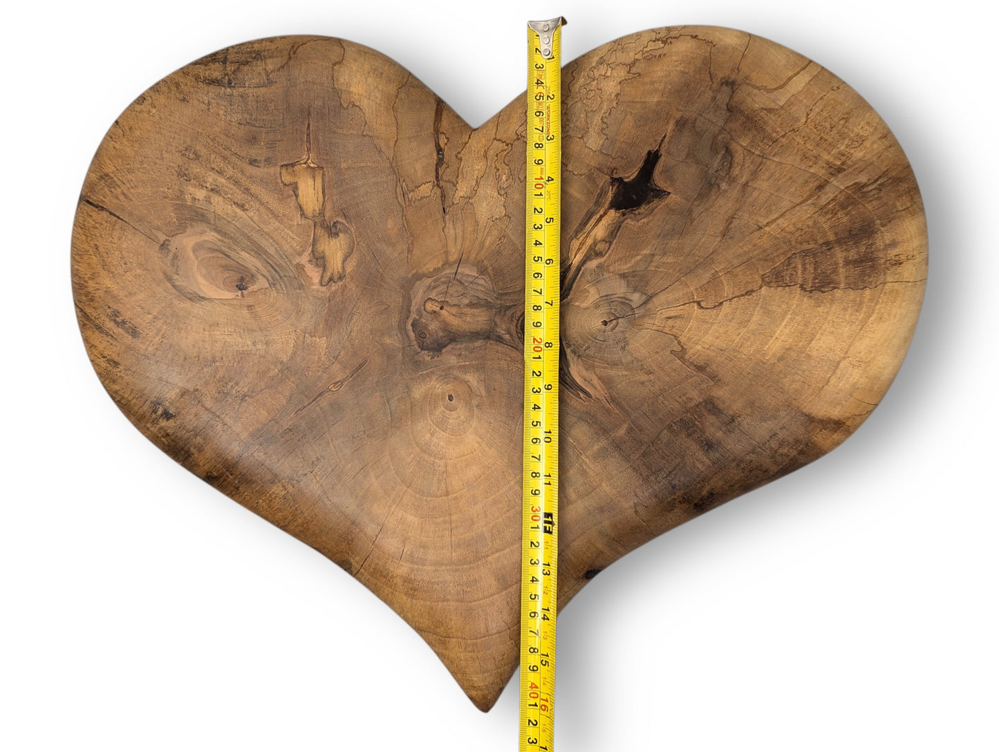 Brown heart-shaped wood slab with visible grain, knots, cracks, and a vertical yellow measuring tape.