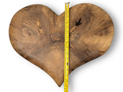 Brown heart-shaped wood slab with visible grain, knots, cracks, and a vertical yellow measuring tape.