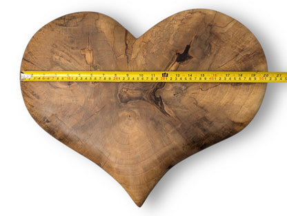 A brown solid hardwood heart with prominent natural grain, knots, and a yellow measuring tape.