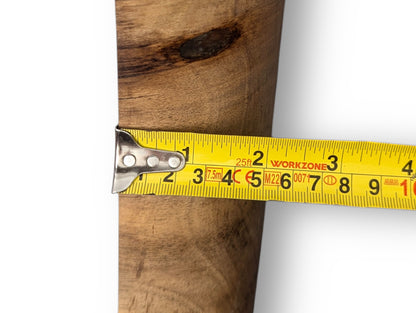 Yellow measuring tape showing units across a natural wood sculpture, displaying prominent grain and a dark knot.