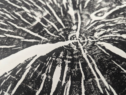 Angled close-up of a black and white print on paper, with textured dark areas and radiating white lines.