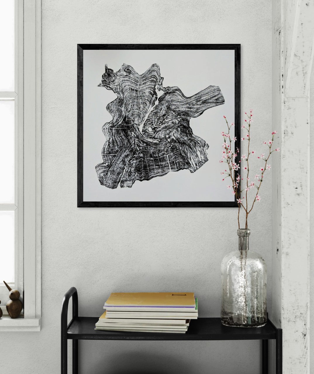 Black framed print of an irregular black tree root impression on white paper, above a shelf.