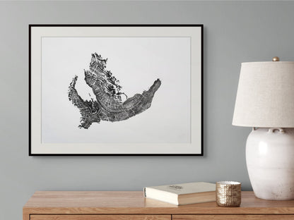 Black framed print of a tree root monoprint with concentric rings, hanging above a wooden side table.